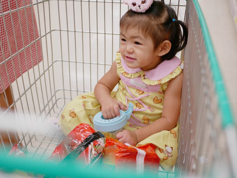 Little Asian baby girl sits in a cart, enjoys doing shopping with her mother.