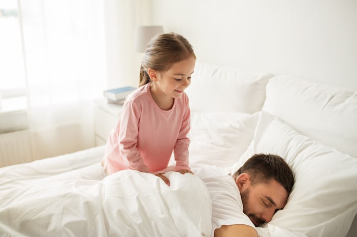 people, family and morning concept - happy little girl waking her sleeping father up in bed at home