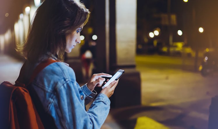 Woman with backpack pointing finger on blank screen smartphone on background bokeh light in night ci...