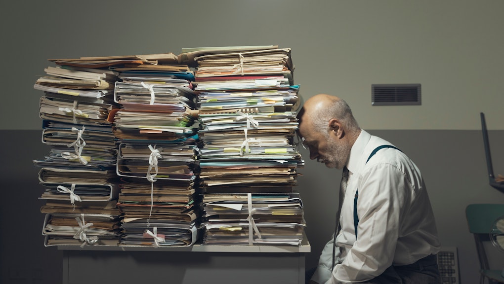 Desperate depressed businessman with lots of paperwork in his messy office at night, he is leaning on a pile of files, bureaucracy and deadlines concept