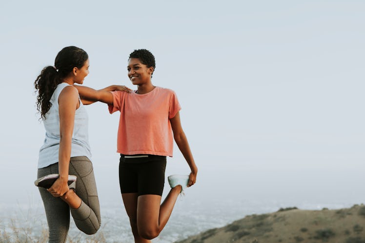 Two friends smile and stretch together in workout clothes outside.