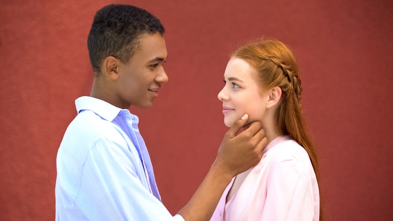 Smiling mixed-race boy tenderly touching chin of his beautiful girl, first love