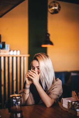 A blonde girl sips pumpkin coffee in a chic restaurant with a yellow wall.