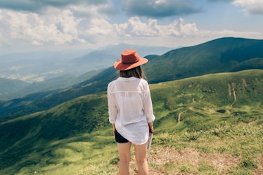 Woman in hat standing back. Mountains background