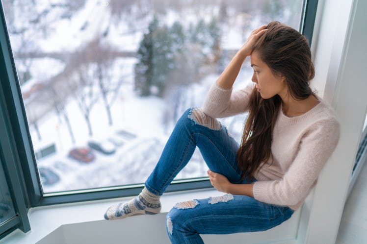 Winter depressed sad girl lonely by home window looking at cold weather upset unhappy. Bad feelings ...