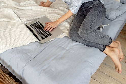 Happy woman with laptop in bed. Girl freelancer works in the home. Female in casual clothes. Online ...
