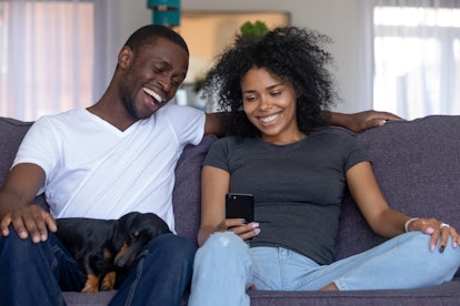 Happy black african couple with pet laughing looking at smartphone taking selfie, having fun in soci...