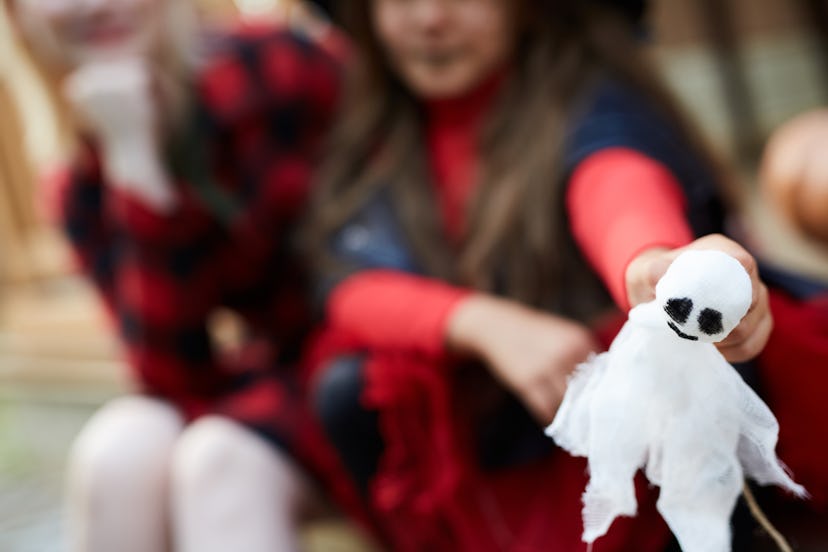 White toy ghost with black eyes held by little girl in halloween attire with her mom near by