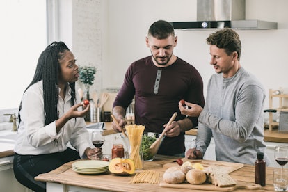 African American woman with two Caucasian men cooking salad together in kitchen at home on weekend