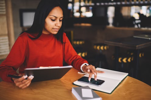 Afro american hipster girl dressed in red sweatshirt checking email on modern telephone device worki...