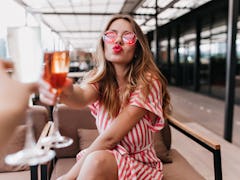 A stylish girl in a striped dress drinks wine with her friend in a rooftop restaurant on a wine vaca...