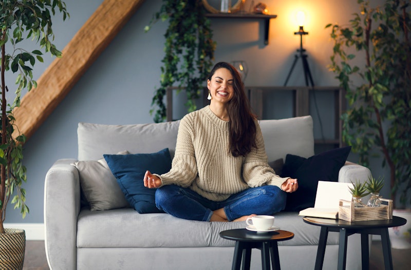 Body and spirit health. Cute smiling woman is learing yoga at home sitting on the sofa