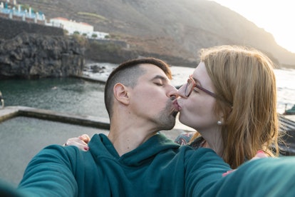 Lovers kissing with passion taking selfie in natural pool. Caucasian blonde girlfriend with glasses ...