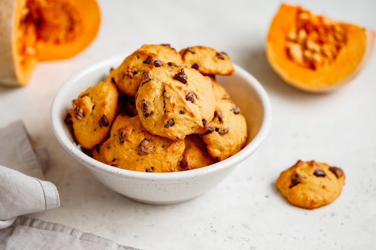 Pumpkin cookies with chocolate chips are placed in a white ceramic bowl with pumpkin slices in the b...