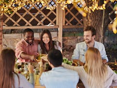 Happy young couple offering their friends traditional food by Thanksgiving table