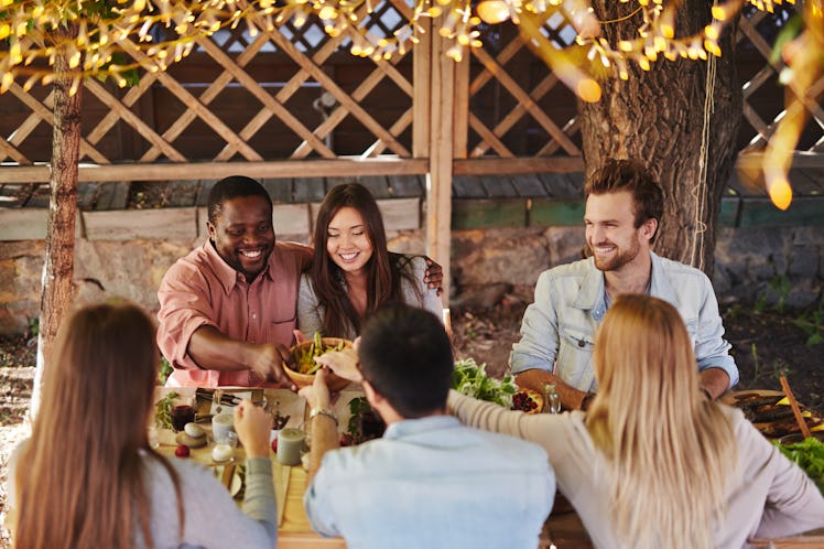 Happy young couple offering their friends traditional food by Thanksgiving table