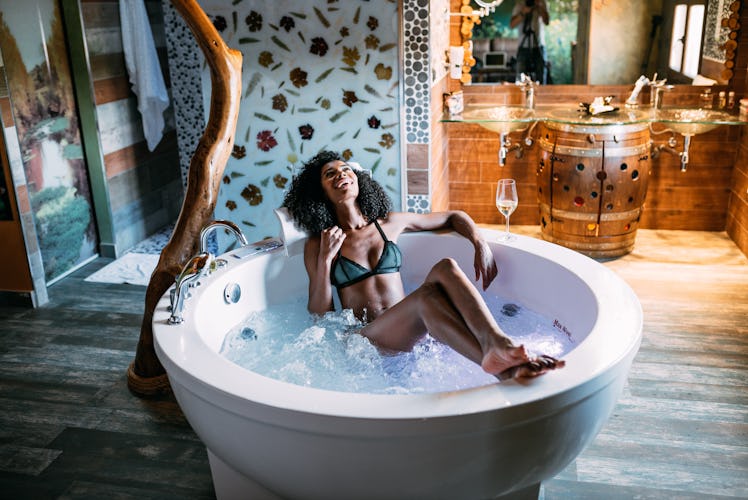 A happy woman relaxes in a hot tub in a hotel room while on a wine vacation.