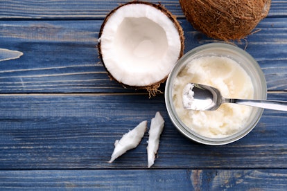 Opened glass jar with fresh coconut oil on wooden background