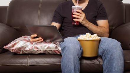 Single man watches movie on digital tablet. They are drinking juice and eating popcorn. Sitting on t...