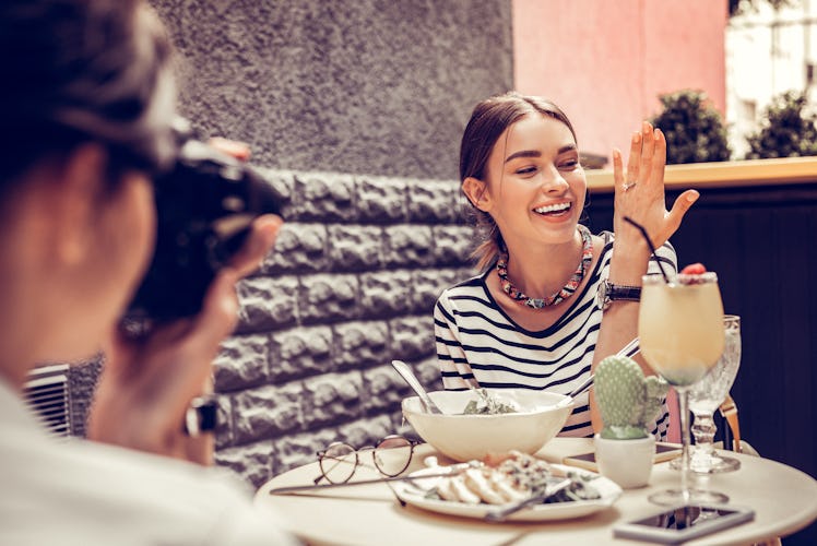 A happy woman smiles for a photo while showing off her engagement ring at brunch.