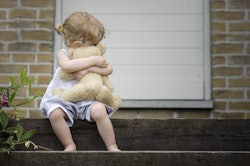 little girl seated on old wooden stairs with teddy bear