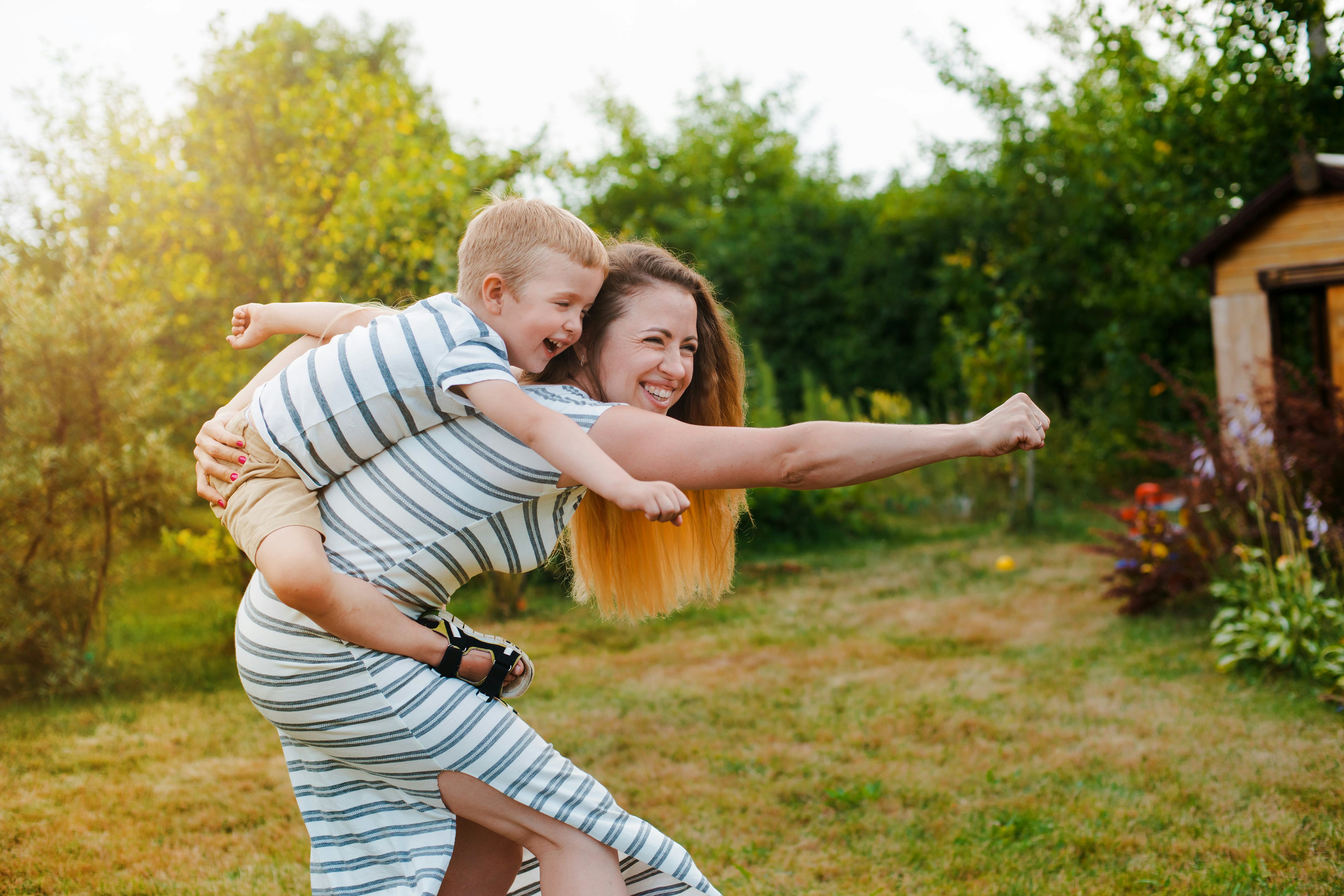 super mom, superman. Happy Caucasian mother and son outdoors in park on sunny spring day. Young brun...
