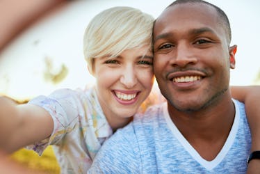 Mixed race couple of millennial in a grass field taking a selfie with a smartphone