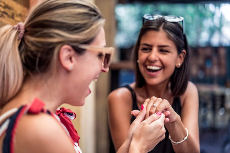 A woman shows off her engagement ring to her friend while smiling.