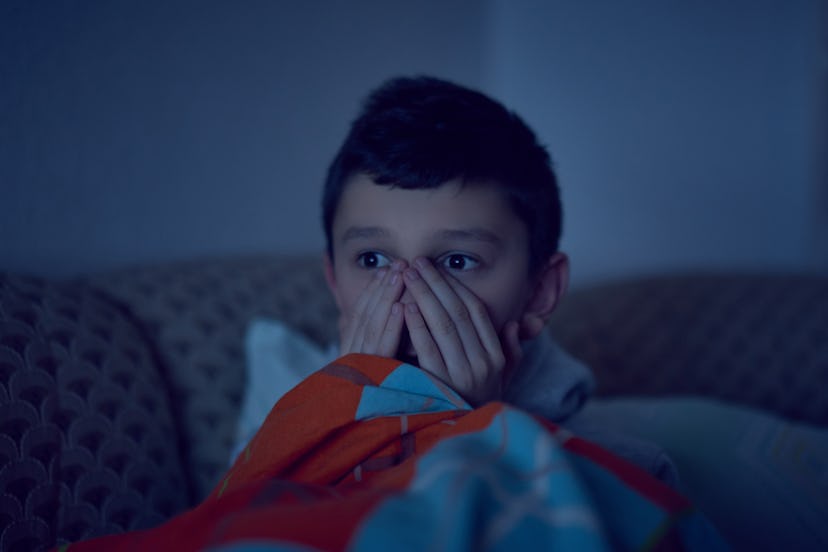 Scared child watching scary movie on tv, sitting on the couch at night
