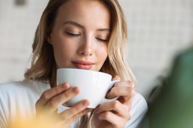 Close up of a beautiful young blonde woman sitting at the cafe indoors, drinking coffee