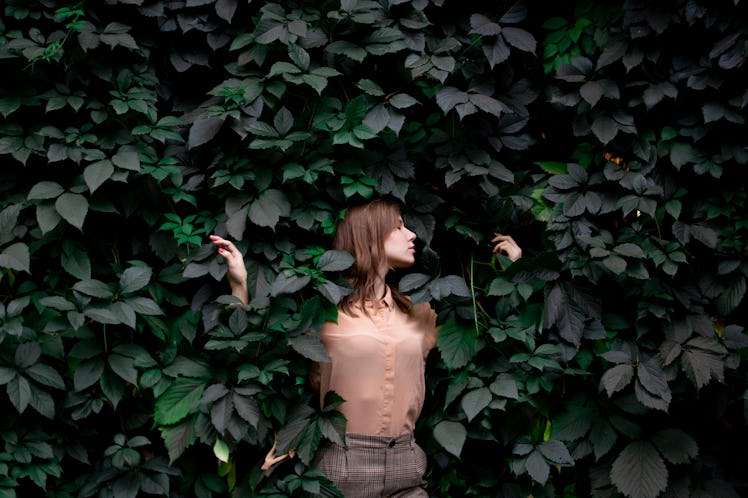 young attractive girl stands in green leaves alone with nature, a woman touches plants and dreams, a...