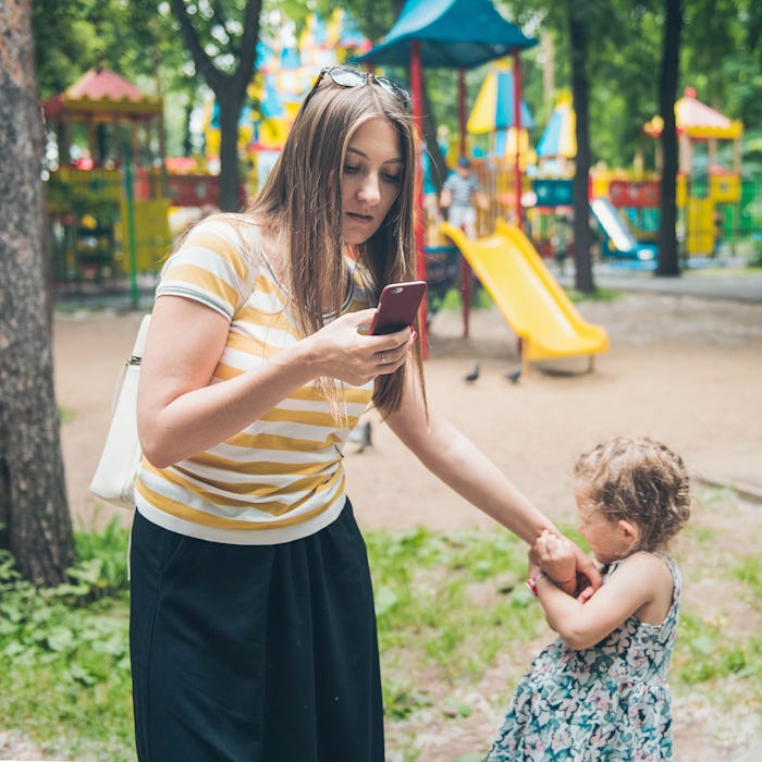 Little girl pulling hand of her mother because her mom surfing Internet on smartphone. Gadgets pro...