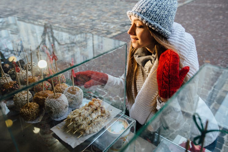 Smiling blond woman is curious looking at the apple candies on the other side of the window, she is ...