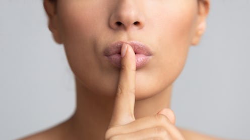 Women's secret. Woman holding finger on lips over grey background