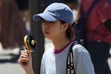 A woman holds a portable fan to avoid the heat in Tokyo, . The mercury is expected to reach 35 degre...