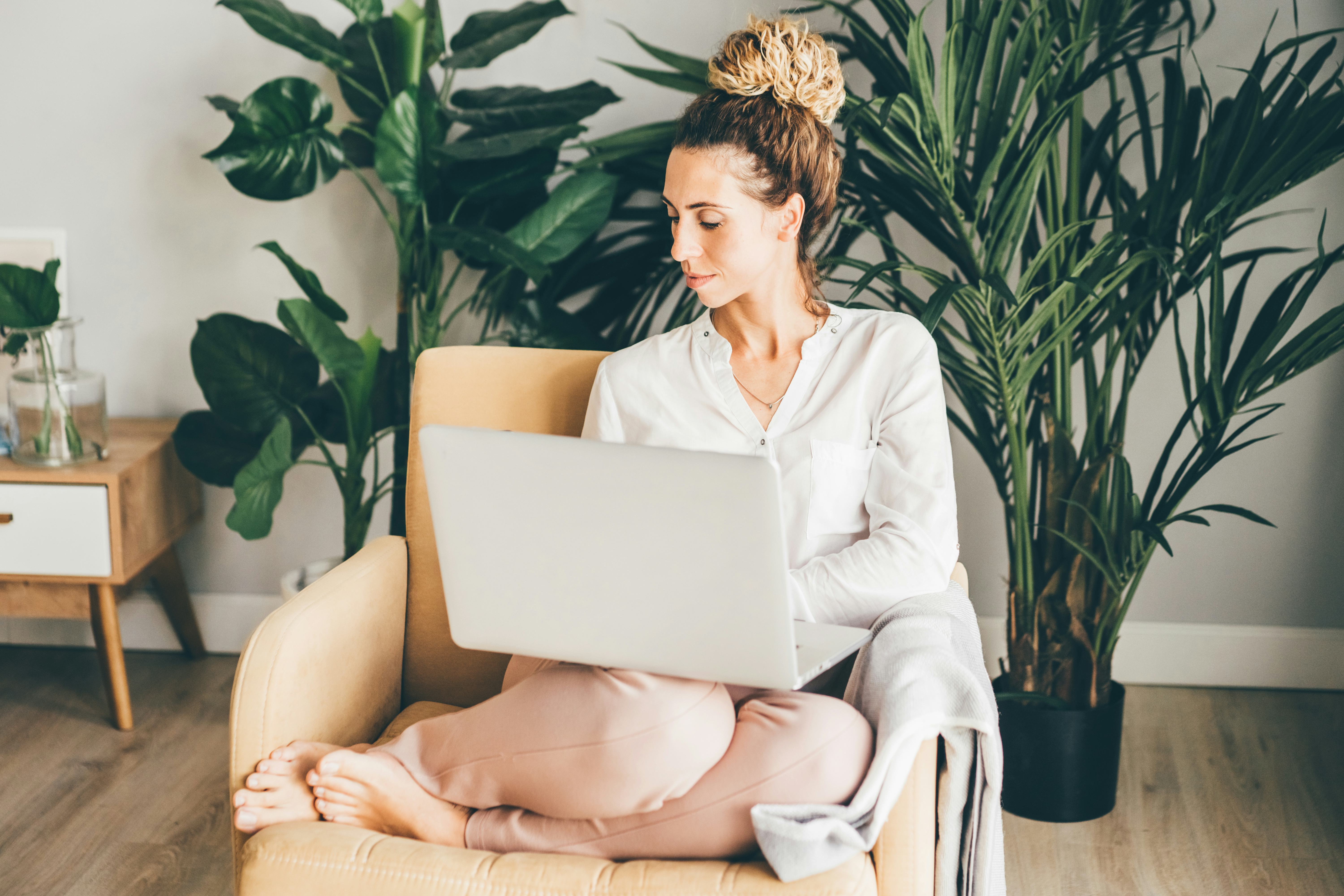 Happy girl sitting on armchair with laptop. Young successful woman working from home.