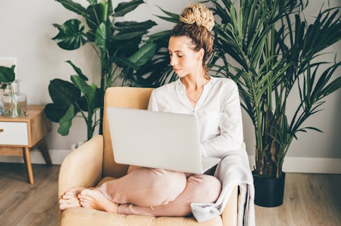 Happy girl sitting on armchair with laptop. Young successful woman working from home.