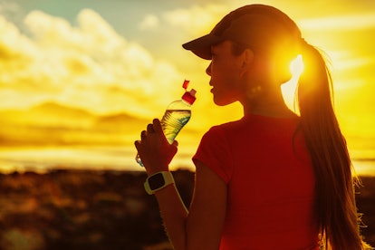 Fitness woman drinking water from sports bottle on afternoon workout after run training jogging outd...