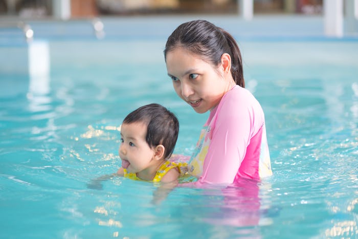 Mother and asian baby girl swimming in a pool, early development class for infants swimming. Baby sw...