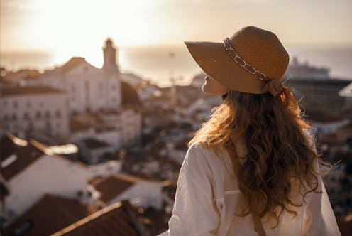 Blonde woman standing on the balcony and looking at coast view of the southern european city with se...