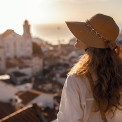 Blonde woman standing on the balcony and looking at coast view of the southern european city with se...