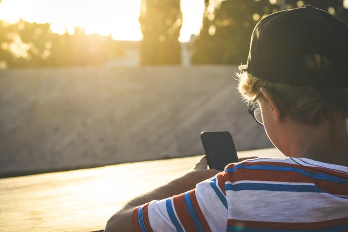 Back view of a beautiful teen using smartphone social app leaning on a concrete wall outdoor Young t...