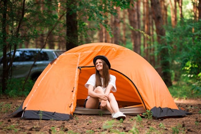 Young woman resting in hat near camping tent in wilderness. Rest concept