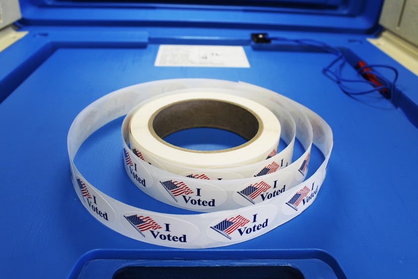 Red white and blue "I voted" stickers with American flag are on a spool of stickers placed on a voti...