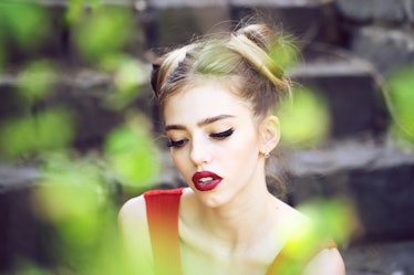 Beautiful sad young woman on a stone stairs and green leaves background posing with red lips