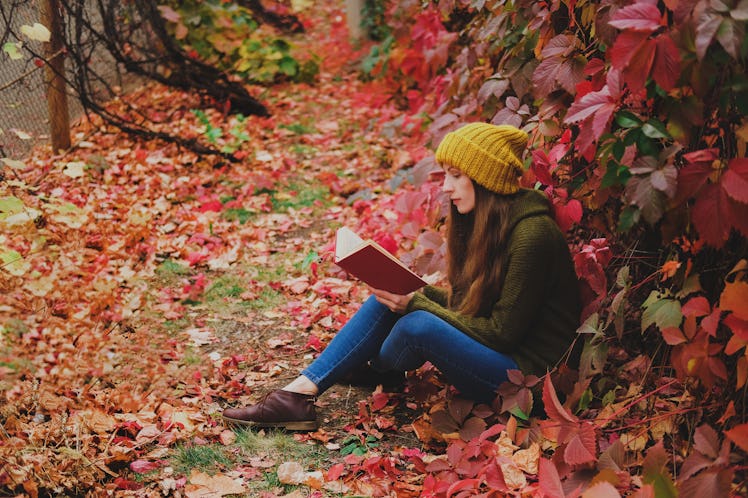 Girl in mustard yellow knit hat and marsh green wool sweater sitting among colorful ivy in autumn an...