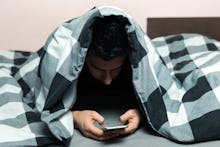 Young man in pajamas using a cellphone while lying in bed.