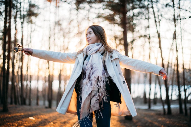 The girl cheerfully turns in the rays of the setting sun. A young woman in a light raincoat is danci...