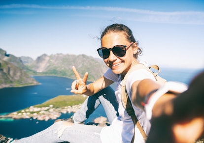 Happy woman hiker doing selfie at the top of Reinebringen hike above Reine village in the Lofoten ar...