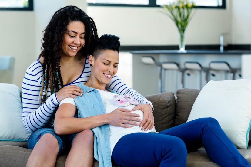 Pregnant lesbian couple sitting on sofa with a pair of pink baby shoes